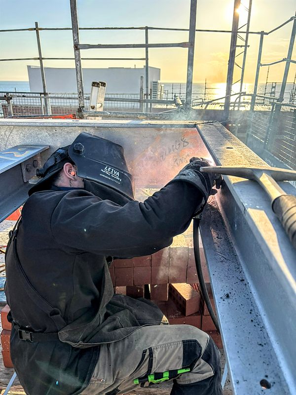 Welder wearing a LEIVA METAL WORKS helmet welding steelwork at sunset