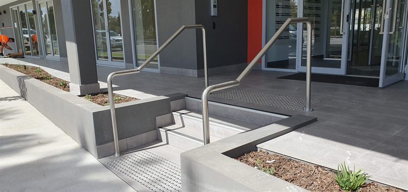 Two metal handrails installed beside outdoor entrance steps