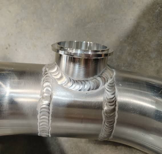 Curved metal pipe with a welded branch fitting and circumferential welds